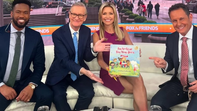 Ainsley Earhardt con un vestido corto morado mientras promocionaba un libro para niños en Fox News