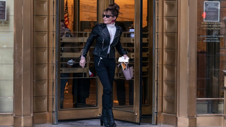 Sarah Palin sale de un edificio con una chaqueta de cuero, pantalones negros, botas de cuero y el pelo recogido.