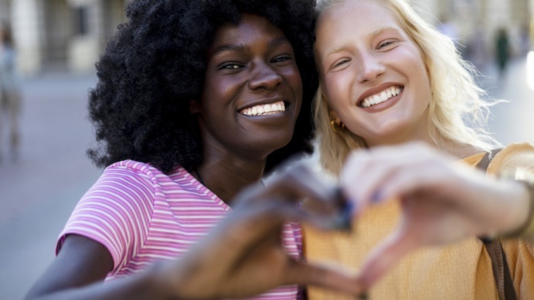 Dos mujeres sonríen, haciendo un corazón con sus manos.