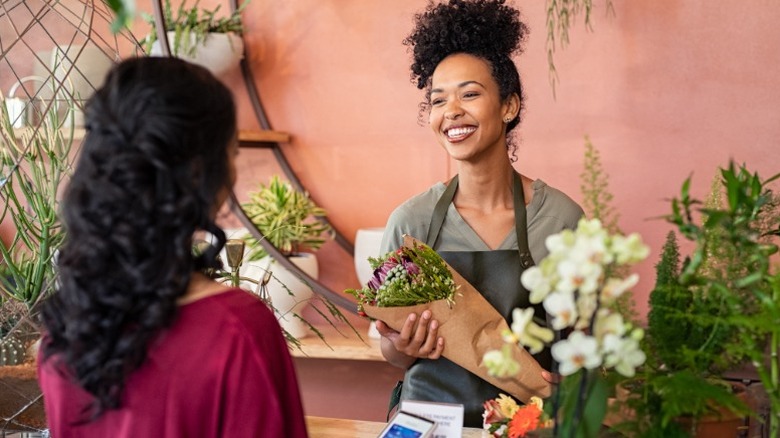 Una mujer compra flores a una floristería sonriente.