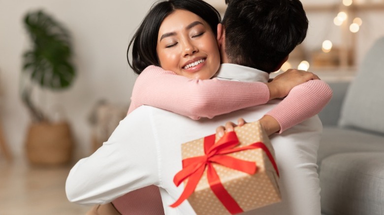 Una mujer sostiene un regalo mientras abraza a un hombre.