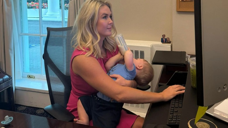 Karoline Leavitt sosteniendo a su hijo mientras mira una computadora