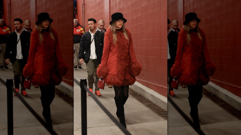Taylor Swift caminando con un abrigo rojo con adornos de piel y botas