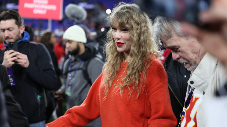 Taylor Swift con pelo rizado y suéter naranja