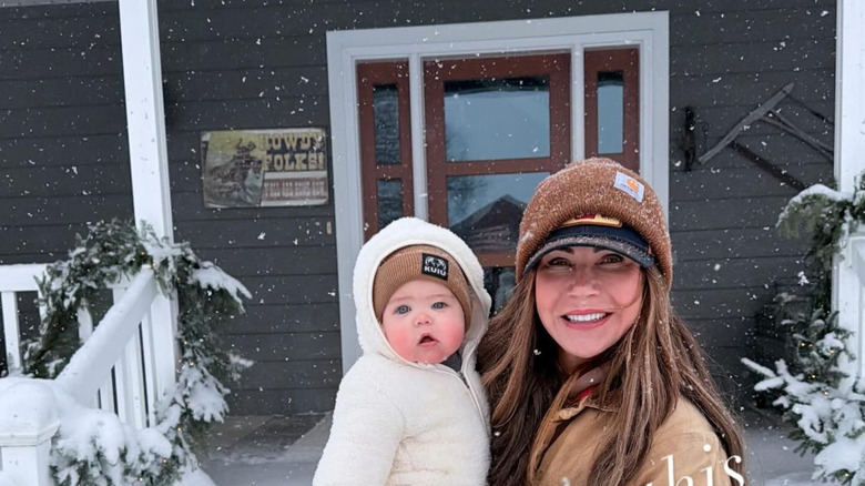 Kristi Noem cargando a un bebé en la nieve sin maquillaje