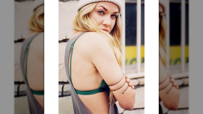Erika Kirk mirando por encima del hombro, vestida con un gorro y una camiseta holgada sobre un sujetador verde.