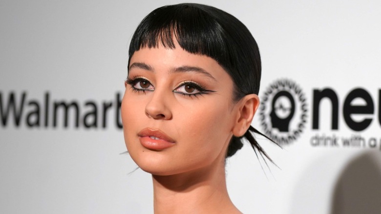 Primer plano de Alexa Demie en un evento en 2020. Lleva una mirada espectacular con delineador de ojos negro grueso y su cabello peinado hacia atrás en un moño; sus microflequillos quedan afuera.