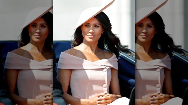 La imagen completa del look Trooping The Colors 2018 de Markle. Ella está sentada en un carruaje con un vestido rosa pálido con hombros descubiertos y sin mangas.