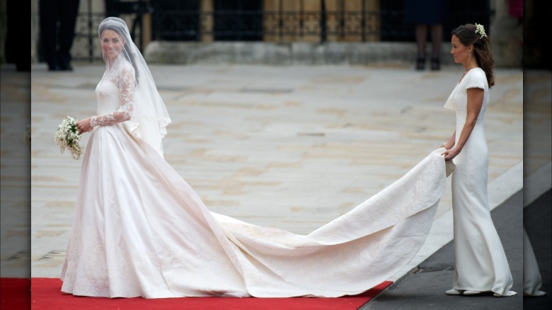 Kate Middleton el día de su boda. Esta imagen ofrece una vista completa de su vestido y su larga cola. Su fino velo blanco cubre su rostro.