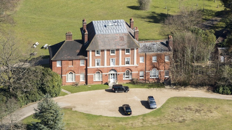 Una imagen de Forest Lodge, el nuevo hogar de Kate Middleton y el Príncipe William. Es una casa grande de ladrillo con muchas ventanas, rodeada de exuberante vegetación.