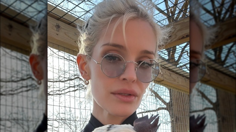 Kelly Osbourne sin maquillaje y con el pelo rubio recogido. Lleva un par de gafas con montura de alambre en forma circular.