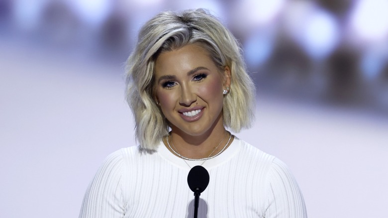 Primer plano de Savannah Chrisley. Lleva la cara maquillada, demasiado arreglada, y una camiseta blanca.
