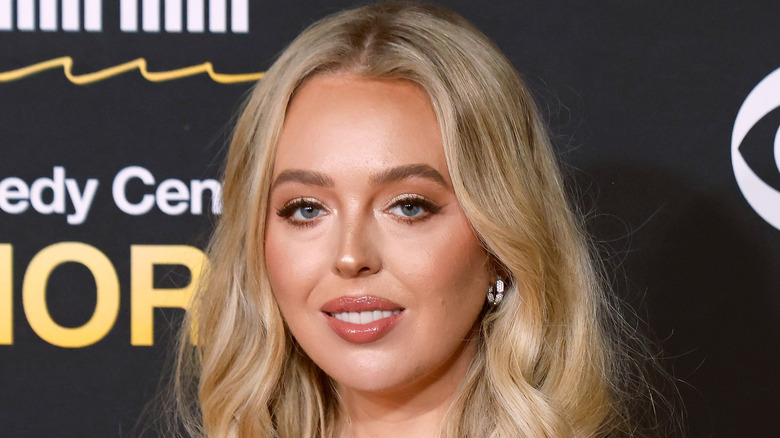 Tiffany Trump con brillo de labios color melocotón posando frente a un fondo negro