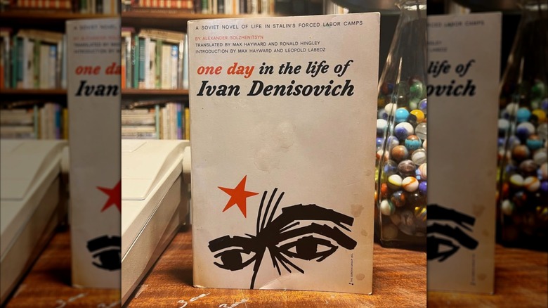 Un libro se encuentra frente a una estantería rústica y una lámpara llena de canicas al fondo.