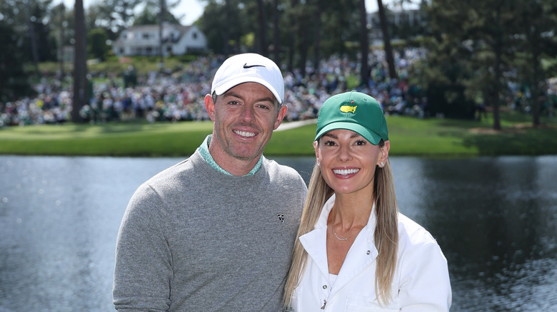 Erica Stoll y Rory McIlroy sonríen frente a un campo de golf con un gran estanque