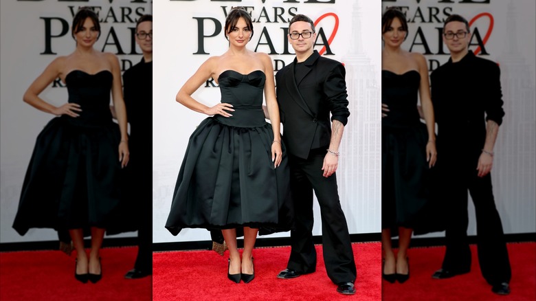 Paige DeSorbo posa con Christian Siriano. DeSorbo es una mujer joven de piel clara y cabello oscuro. Lleva un vestido negro sin mangas con una falda de corte A con cintura caída. Christian Siriano es un hombre de piel pálida y cabello corto y oscuro. Lleva un traje negro con mangas arremangadas hasta los brazos.