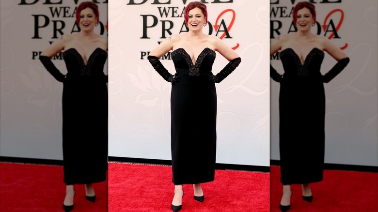 Rachel Bloom en el estreno de DWP2. Es una mujer de piel clara, cabello teñido de rojo y figura más completa. Lleva un vestido negro sin tirantes con un escote pronunciado y guantes de ópera negros transparentes.