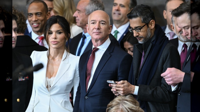 Imagen completa de Lauren Sanchez Bezos y Jeff Bezos en la toma de posesión presidencial de 2025. Lleva una chaqueta blanca con un sujetador de encaje blanco debajo. Lleva un traje azul marino oscuro con camisa blanca y corbata roja oscura.