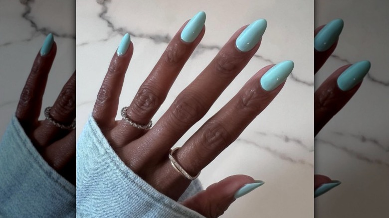 Una manicura azul brillante en una mano con anillos.