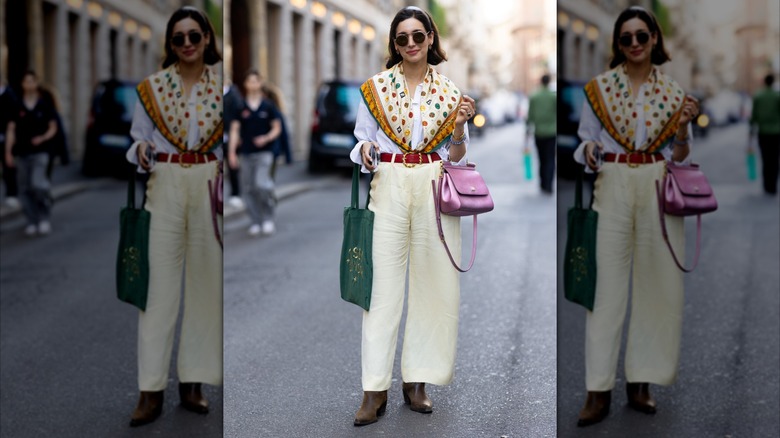 Una mujer posa con una blusa con botones, pantalones color crema y una bufanda estampada.