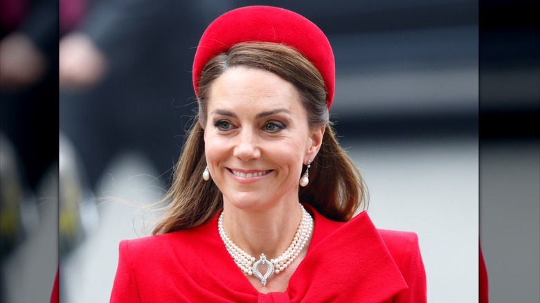 Kate Middleton sonríe mientras camina por la calle con un conjunto rojo y una gargantilla de perlas al cuello
