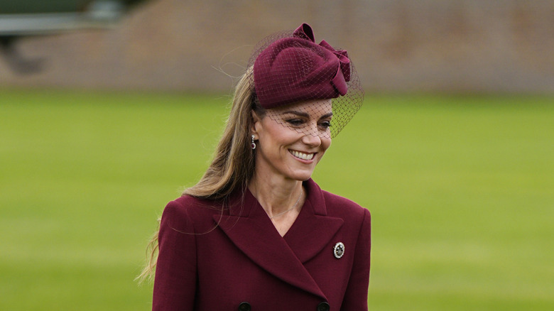 Kate Middleton sonríe mientras camina con un broche en su abrigo color arándano