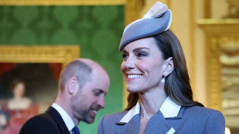 Kate Middleton con un tocado y un traje gris a juego con un maquillaje suave y glamoroso