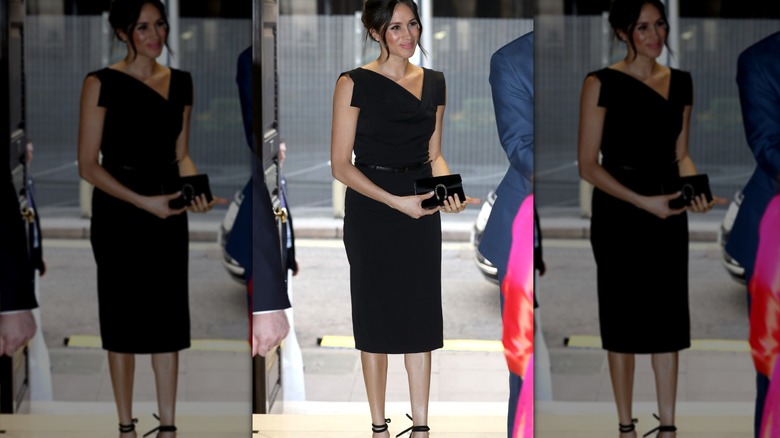 Meghan Markle luce un elegante vestido midi negro y lleva un bolso de mano