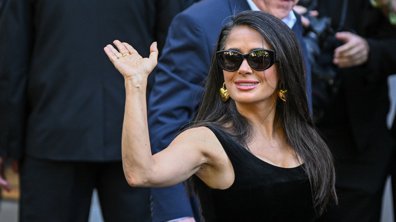 Salma Hayek saludando con sus grises al descubierto y gafas de sol