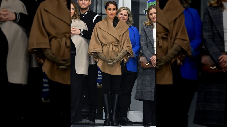 Meghan Markle vistiendo una capa marrón claro con pantalones negros a medida y botas altas de cuero en el evento Invictus One Year to Go.