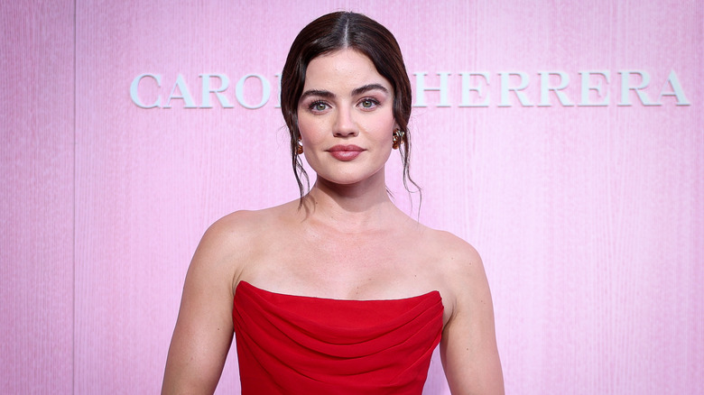 Lucy Hale luce un vestido rojo sin tirantes mientras posa frente a un fondo rosa