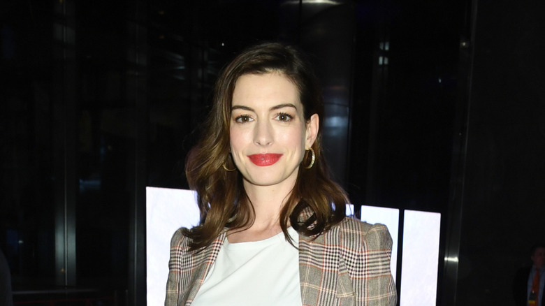 Anne Hathaway posando con una chaqueta a cuadros con labios rojos en 2019.