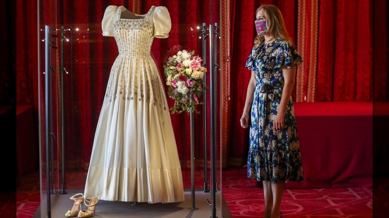 La princesa Beatriz posa junto a su vestido de novia expuesto en el Castillo de Windsor.