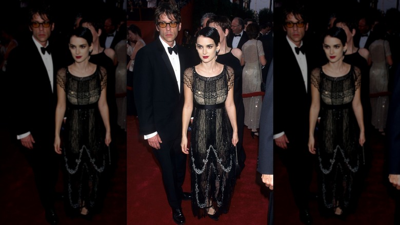 Winona Ryder posando en una alfombra roja con un vestido negro adornado y el pelo peinado hacia abajo.