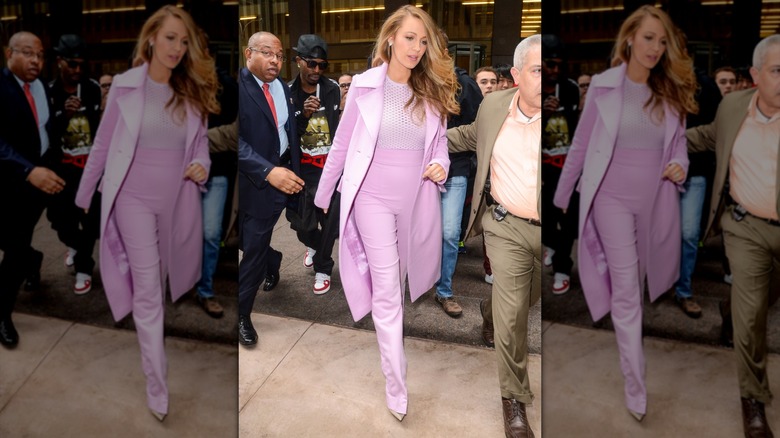 Blake Lively caminando con un traje rosa que consta de pantalones de cintura alta, una blusa de rejilla y un abrigo a juego.