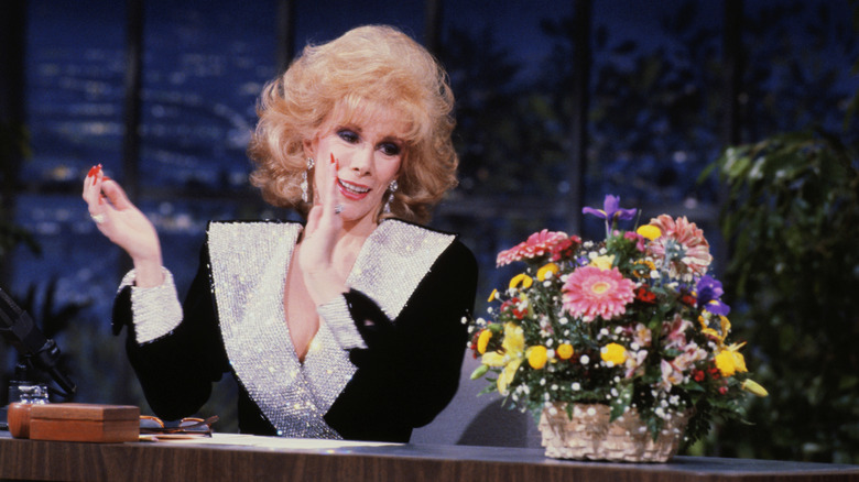 Joan Rivers aplaude mientras mira un ramo de flores en un espectáculo nocturno.