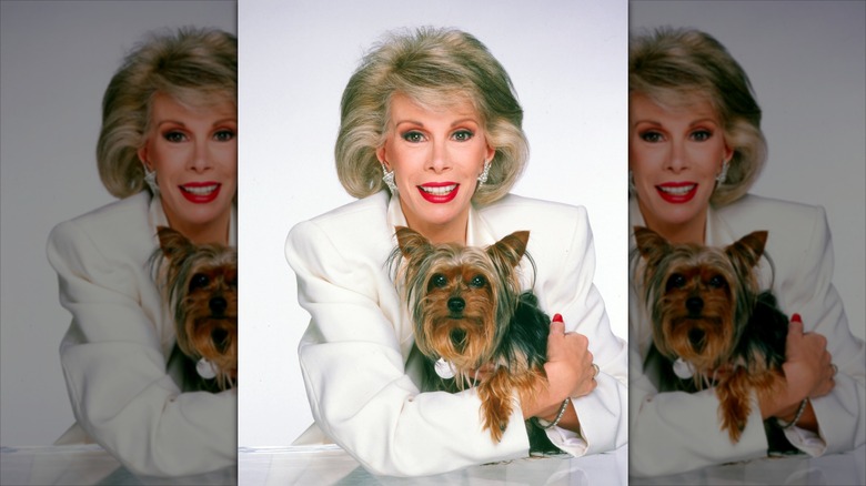 Joan Rivers sonríe con un traje blanco mientras sostiene a un perro.