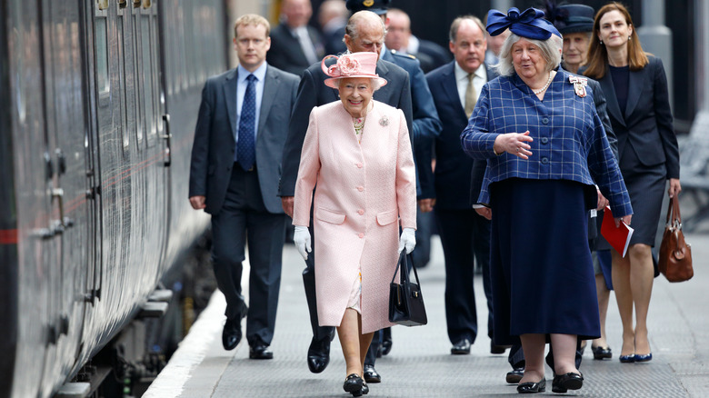 La reina Isabel destaca vestida de rosa pálido entre una multitud