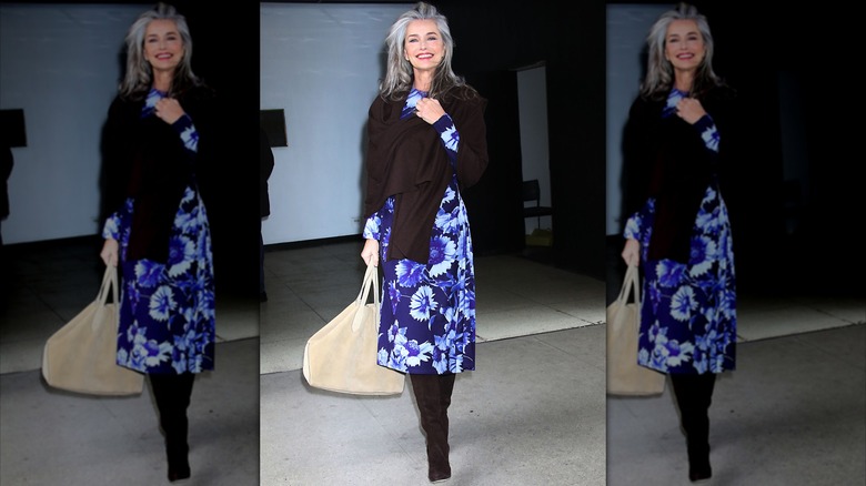 Paulina Porizkova caminando con un vestido floral azul y un suéter y botas negros.