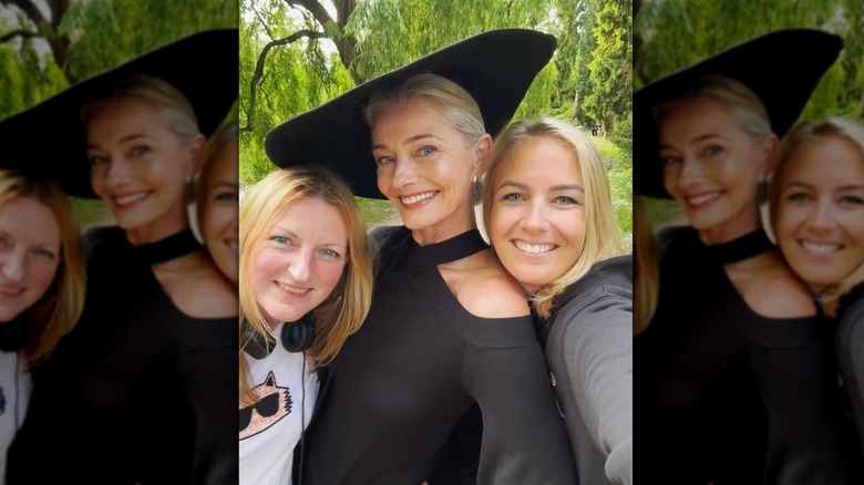 Paulina Porizkova posa afuera junto a dos mujeres rubias para una selfie con un vestido negro y un sombrero plano.