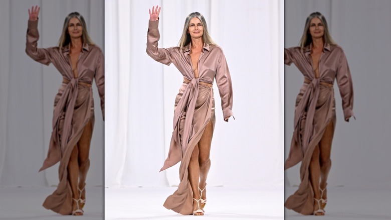 Paulina Porizkova caminando por la pasarela con un vestido sedoso beige en un desfile de Balmain.