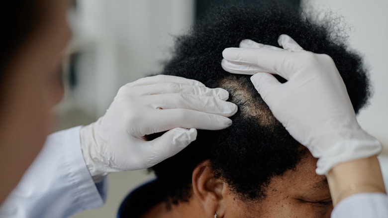 Doctor examinando el cabello y el cuero cabelludo de la mujer