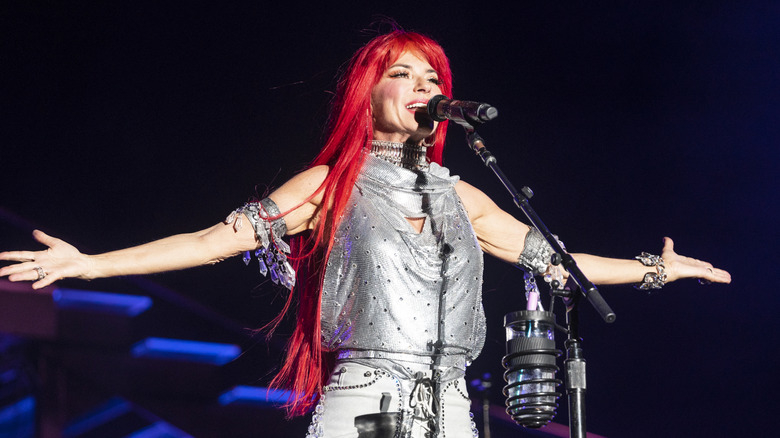 Shania Twain actúa en el escenario con una peluca roja brillante y una blusa sin mangas plateada metálica.