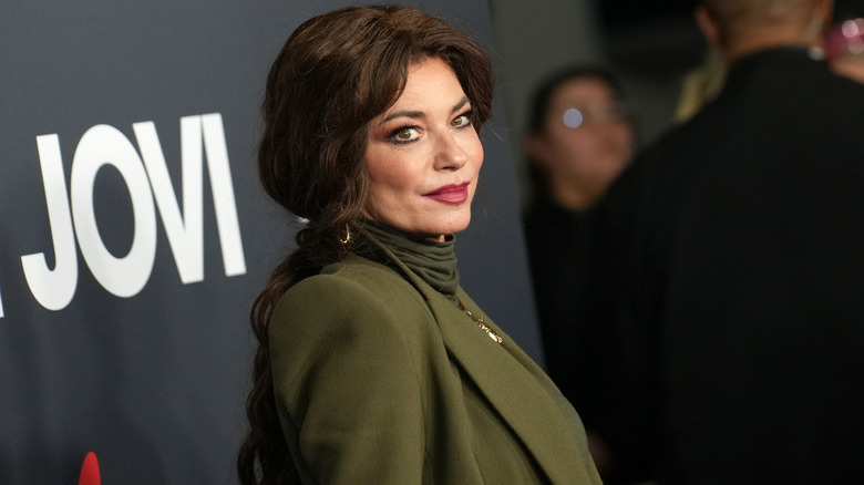 Shania Twain viste un jersey de cuello alto verde oliva y una chaqueta a juego con el cabello castaño oscuro peinado en una trenza.