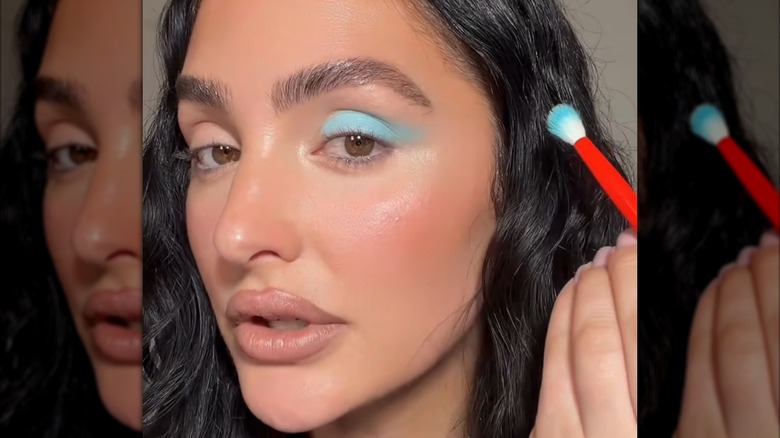 Imagen fija de un tutorial de maquillaje de una mujer que se aplica una sombra de ojos azul brillante.