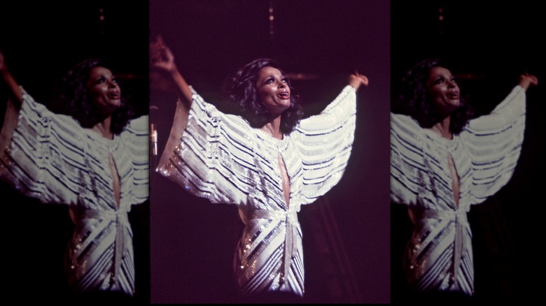 Diana Ross actuando con los brazos en alto y luciendo un vestido fluido de rayas blancas y negras.