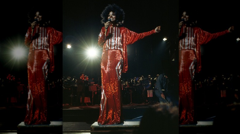 Diana Ross actúa en el escenario vistiendo un traje rojo y blanco brillante con un gran peinado afro.