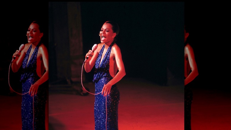 Diana Ross cantando frente a un micrófono en el escenario con un vestido azul brillante.