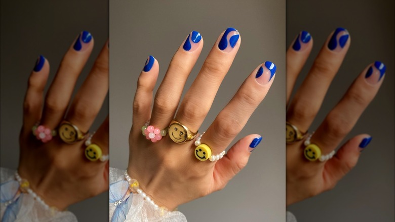 Primer plano de una manicura azul ondulada en una mano con varios anillos estilo años 60.