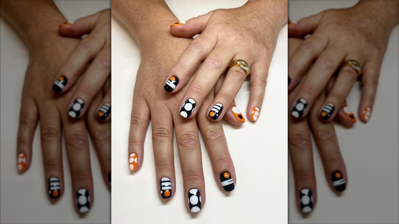 Mira de cerca una manicura estilo Mod con formas geométricas en negro, blanco y naranja.